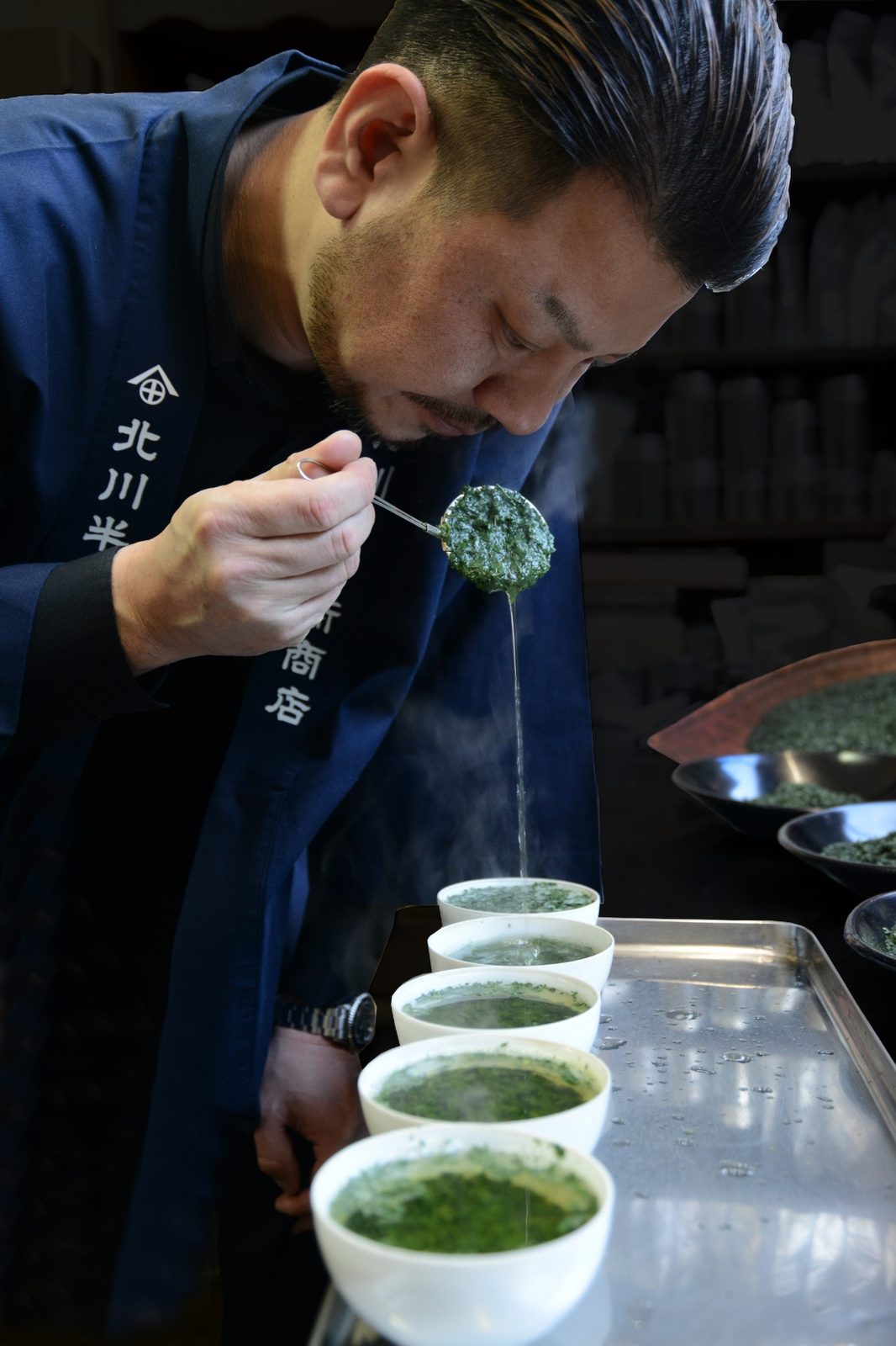 Tea master tasting steeped tea from white cups with steam rising
